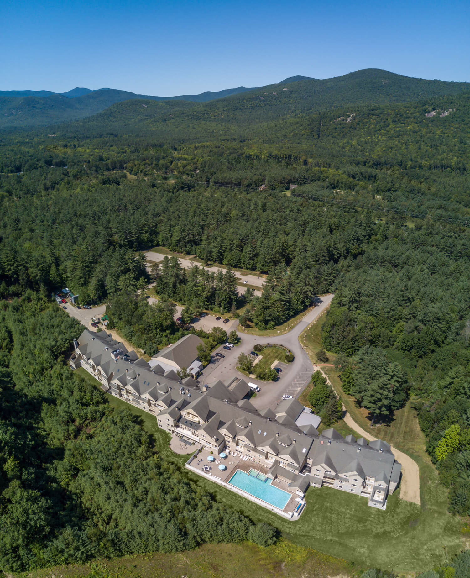 Forest-framed aerial of Grand Summit Attitash in Bartlett, New Hampshire, showcasing a sprawling mountain lodge with pool and views of the surrounding peaks