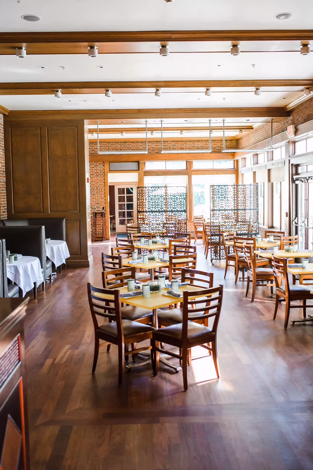 Spacious hotel dining area with hardwood floors, sunlit windows, and neatly arranged tables in a bright restaurant setting
